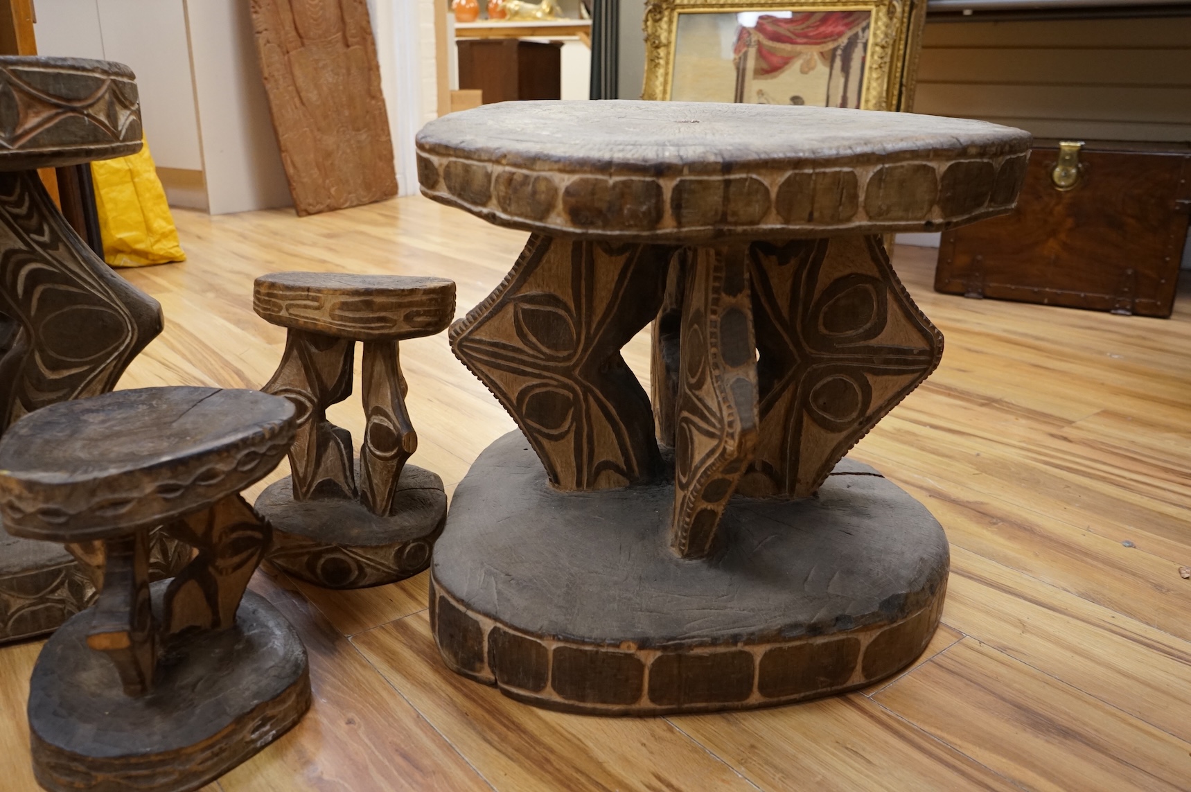Papua New Guinea Sepik River, two tribal tables, each carved from a section of tree trunk, with circular top and base, the supports and edges incised and painted with geometric designs and two other small stools, largest